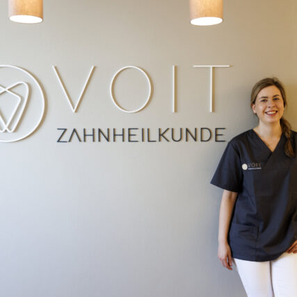 Katharina Voit steht an der Wand neben Praxislogo in 3D